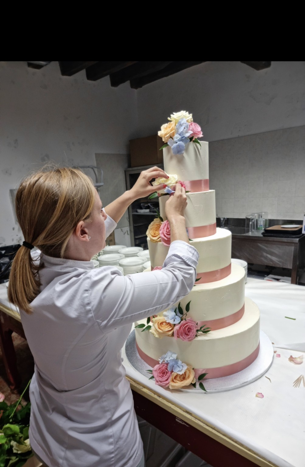 Elisa Fornasiero decora una torta a piani con fiori e nastri rosa