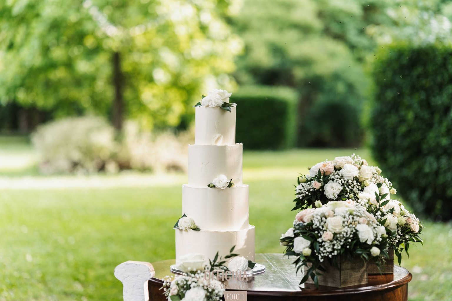 Torta nuziale bianca a quattro piani con fiori bianchi nel giardino di La Calendula
